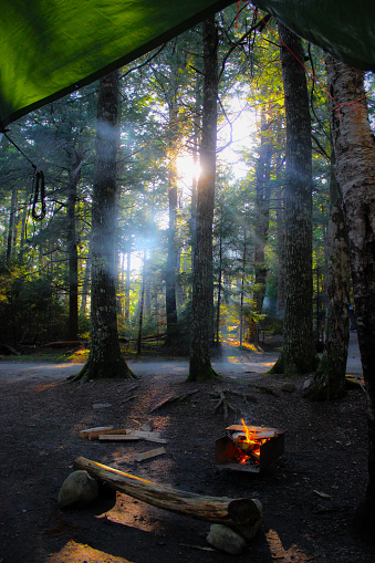Sunbeam shining through the trees and the smoke from the fire in a firebox during a camping trip in Kejimkujik National Park, Nova Scotia, Canada.