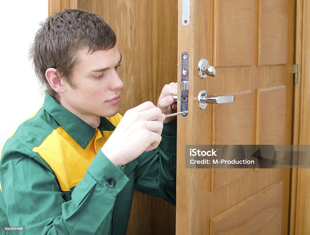 Young handyman in uniform changing door lock Adult Stock Photo