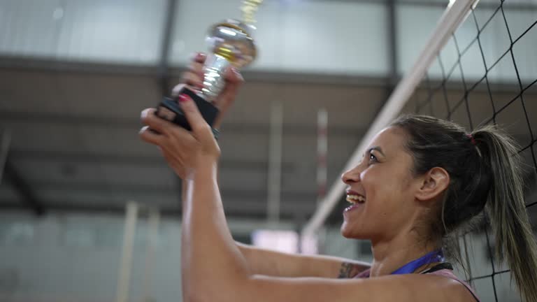 Mid adult female volleyball player kissing the trophy on the sports court