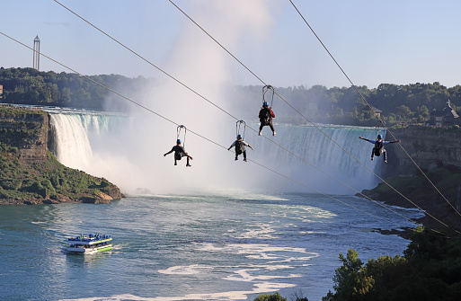 Niagara Falls, Ontario, Canada - August 27, 2023: Tourists enjoying zipline ride at Niagara Falls in summer, including Maid of the Mist boat and Horseshoe Falls.