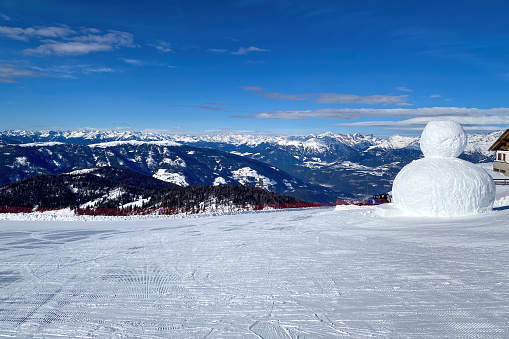 Panoramic view from top of Kronplatz mountain (ital. Plan de corones) with giant snowman against blue sky with clouds