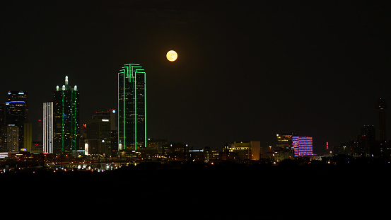The August 30, 2023 supermoon emerges from behind the Bank of America Plaza in downtown Dallas.
