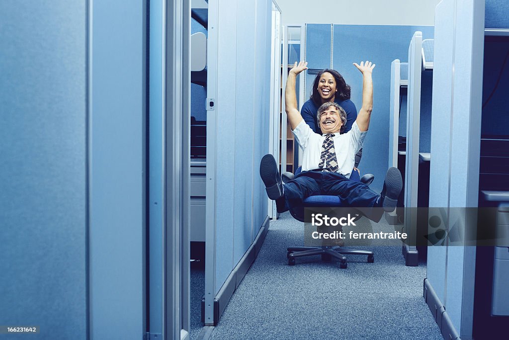 Office Party Co-workers racing through cubicles with office chair. Humor Stock Photo