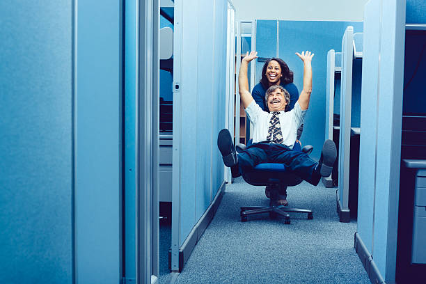 Office Party Co-workers racing through cubicles with office chair. office cubicle photos stock pictures, royalty-free photos & images