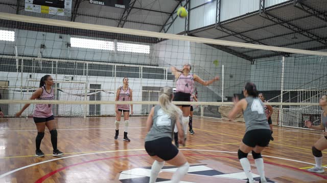 Female volleyball player spiking the ball while other team defending at sports court