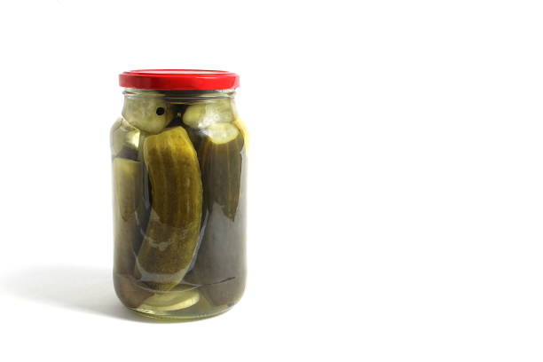 A glass jar with pickles stands on a white background.