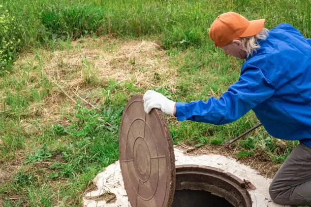 Photo of A plumber opens a manhole cover on a concrete well. Inspection and maintenance of water and sewer wells