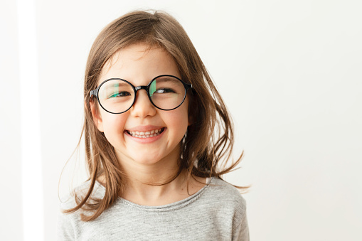 Little girl with eyeglasses is smiling at camera.