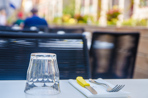 Close up on outdoor dining table with drinking glass, fork, knife and napkin on a restaurant patio downtown Old Quebec during summer day