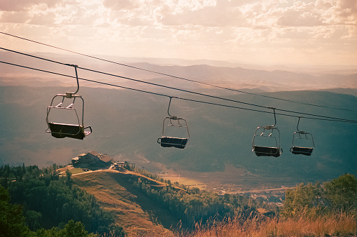 Empty chairlifts at ski resort in the fall await the winter ski season with sun setting in background.