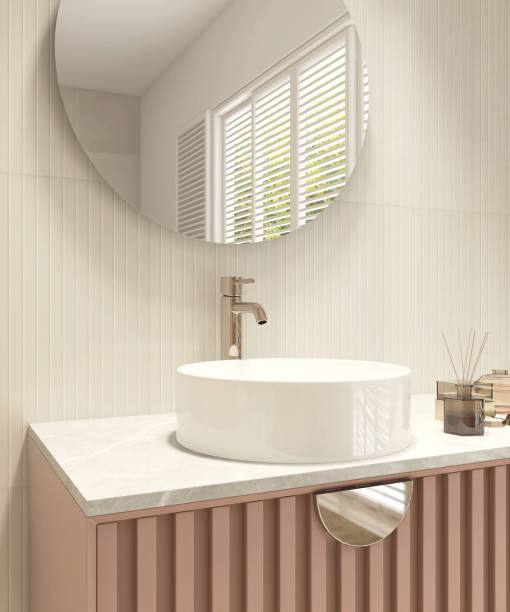 istock Reed stick diffuser, white round washbasin on marble vanity countertop, pink corrugated counter, round mirror in cream wainscot wall bathroom in sunlight from window blinds 1662509208