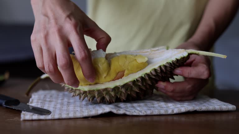 A cropped image of a woman's hand is seen showing a freshly opened durian fruit at home.