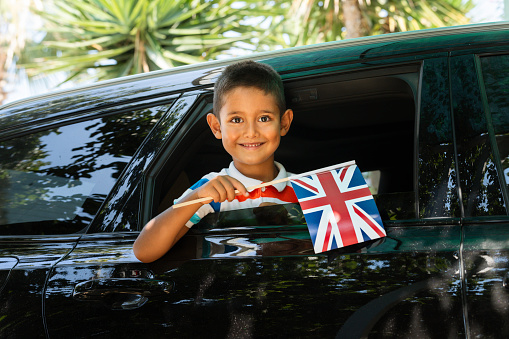 Little Boy in car is holding British flag with a cute smile.