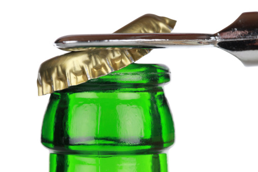 Opening a green beer bottle with an opener, isolated on white background