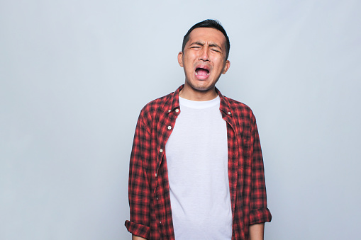 Asian young man wearing flannel shirt with cry expression.