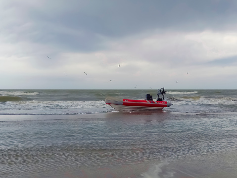 Rigid hull inflatable boat with outboard motor in the shore beaten by the waves. Sea fishing