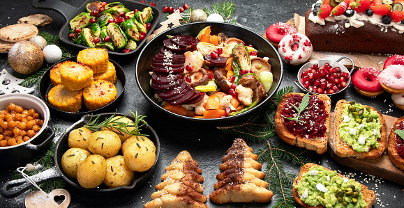 Vegan food with brussels sprouts, carrots, cauliflower, mushrooms, avocado, cake on a dark background, top view. Vegetarian Christmas dinner, healthy food.