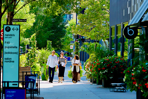 Fairfax, Virginia, USA - September 5, 2023: A mature couple walk with a sales associate for Modera Mosaic Apartments through the heart of the Mosaic District on a hot, summer afternoon.