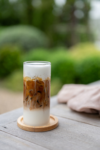 Close-up image of an iced macchiato on a wooden table in a beautiful garden. cold drinks, coffee shop drink, summer