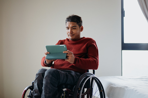 Disabled asian man in a wheelchair using digital tablet at home