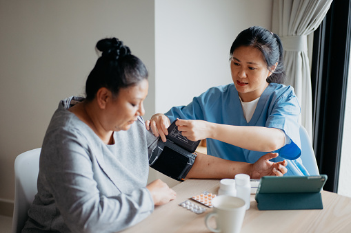 Home caregiver measuring blood pressure of a female patient at home