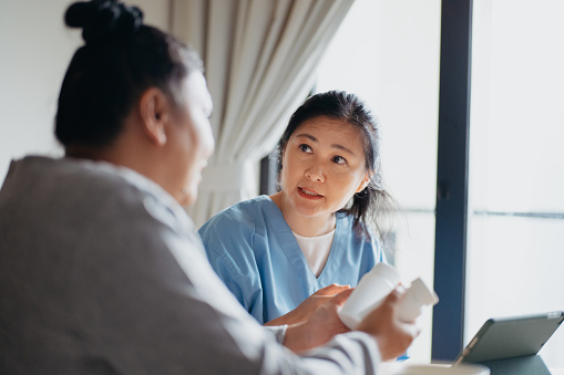 An Asian Chinese female doctor explaining about medicine info to her senior patient during a healthcare house call