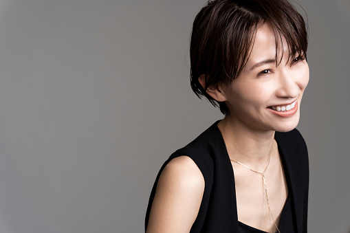 A Japanese woman with short hair wearing a black top and accessories.Gray background studio shot.