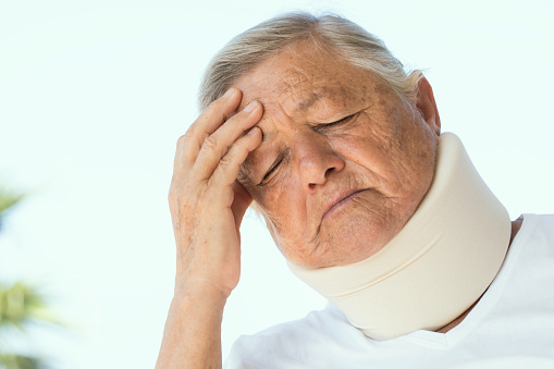 Senior woman wearing neck brace is touching her head in pain with closed eyes.