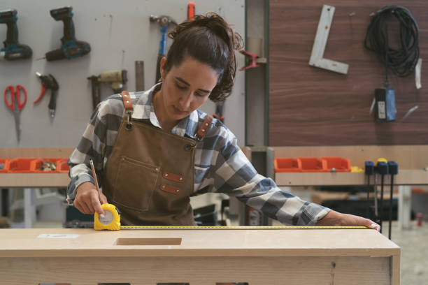 istock Female carpenter using measuring tape at carpentry workshop. Joiner female working with tape measure in wood factory 1662685774