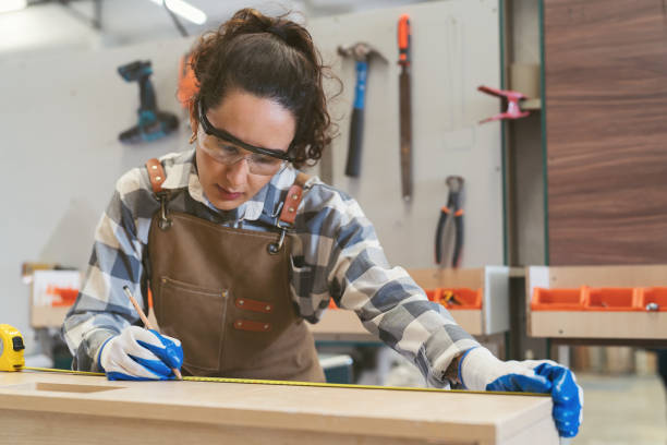 istock Female carpenter using measuring tape at carpentry workshop. Joiner female working with tape measure in wood factory 1662686112