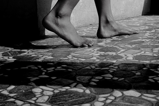 A pair of female child's feet stepping on a stone-patterned floor.