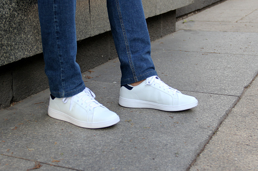 close-up of a woman's feet in jeans and sneakers tripping over unevenly laid paving slabs. Accident, injury on a walk due to poor road surface.