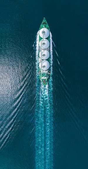 Aerial top view LNG Tanker ship (Liquified Natural Gas) with contrail in the ocean sea ship carrying container and running for export from container international port to custom ocean concept freight shipping by ship service