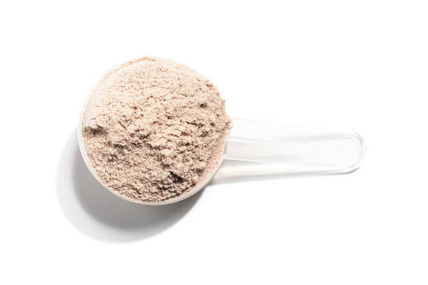 Chocolate whey protein powder in a plastic measuring spoon, isolated on white background, top view