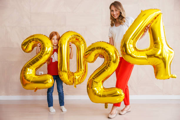 Mother and daughter holding giant balloons shaped as numbers 2024 representing upcoming New Year stock photo