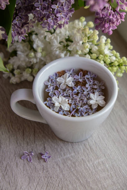 istock Tasty black tea in white cup on windowsill with aromatic lilac flowers. Spring composition Cup of lilac tea drinking recipe flowering branches of purple lilac. Still life for copy space greeting card, poster, banner, wallpaper 1662842325