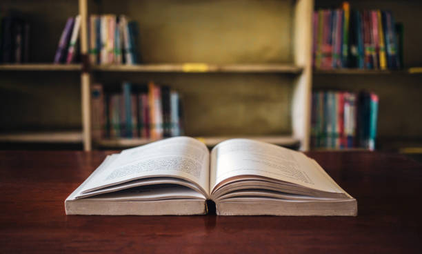 istock On a wooden table, there's an open book with a library visible in the background. A stack of books nearby adds to the theme of educational learning. 1662849893