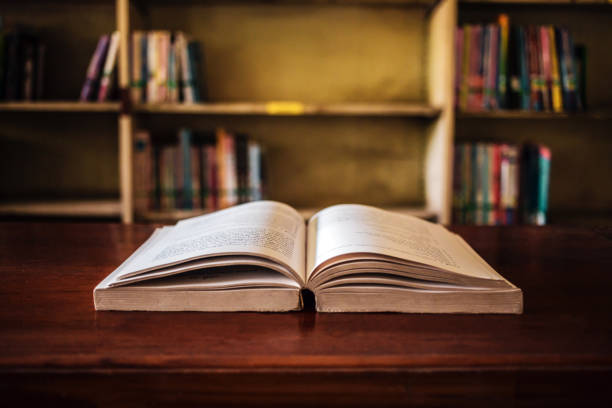 istock On a wooden table, there's an open book with a library visible in the background. A stack of books nearby adds to the theme of educational learning. 1662849896