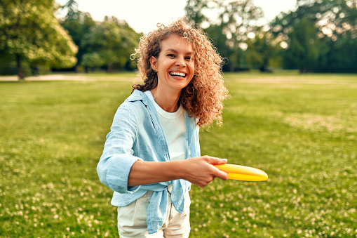 Happy young woman playing frisbee in a meadow in the park, having fun on a warm sunny day off.