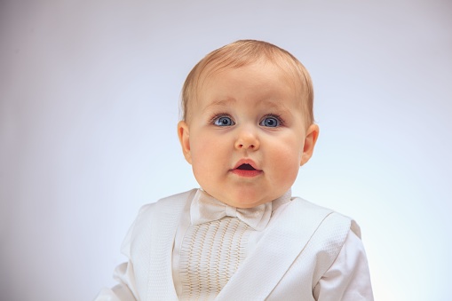 An infant wearing a white tuxedo and a bow tie against a white background.