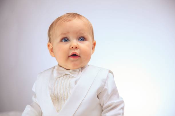 An infant wearing a white tuxedo and a bow tie against a white background.