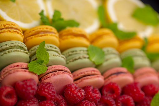 macaroons of different colors with with raspberries, lemon and mint