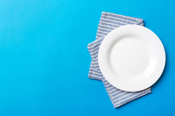 istock Top view on colored background empty round white plate on tablecloth for food. Empty dish on napkin with space for your design 1662887895