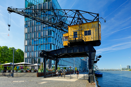 The revitalized Rheinauhafen urban district along the former industrial port of Cologne. Located in the south of Cologne, various modern office buildings line up along the Rhine. A pedestrian promenade invites you to take a stroll. A restored crane points to the history of the place.