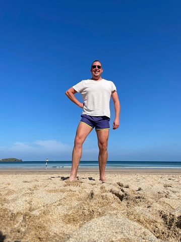 A male wearing short shorts enjoying the sunshine on a beach.