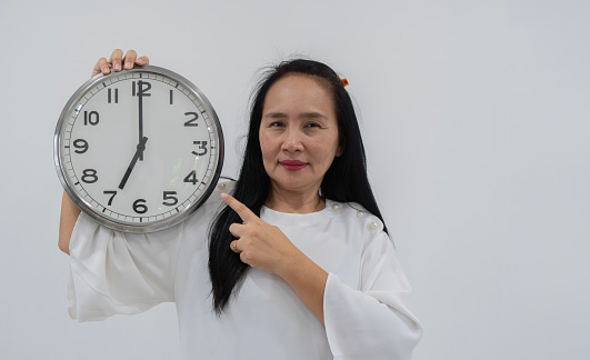 Photo of happy Asian lady point clock wear white dress isolated on white color background. Concept of time management and copy space.