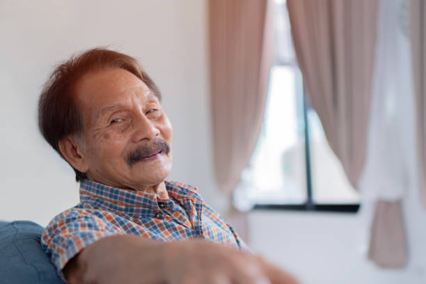istock Satisfied old man looking at camera and smiling while sitting on sofa near the window. 1662909203