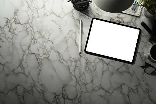 Digital tablet with white screen, glasses, notepad and coffee cup on marble background. Space for text.