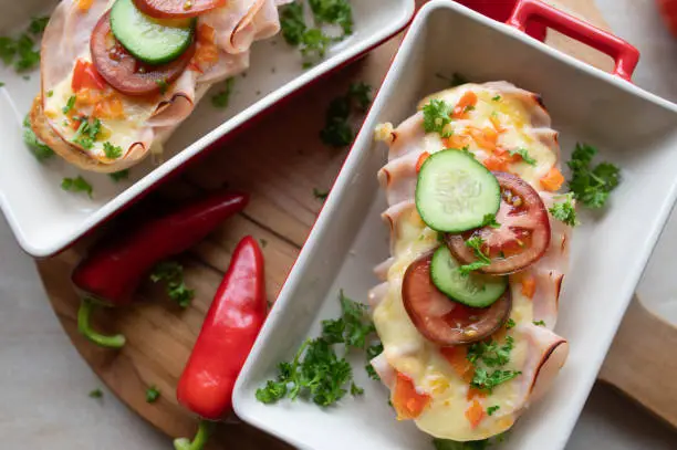 Homemade open faced sandwich with thin sliced turkey breast, cheddar cheese, peppers, tomatoes and cucumber. Served hot and ready to eat on a table. Top view