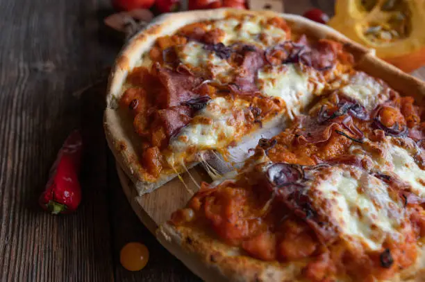 Homemade pizza salami with chunky pumpkin sauce, red onions and mozzarella cheese. Served whole and ready to eat on rustic and wooden table background. Delicious autumn food